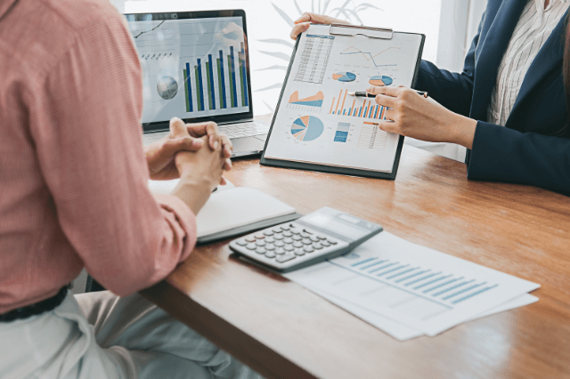 traducción-empresarial-corporativa-inglés-español Dos personas en una oficina, analizando gráficos y datos financieros en una reunión de negocios.